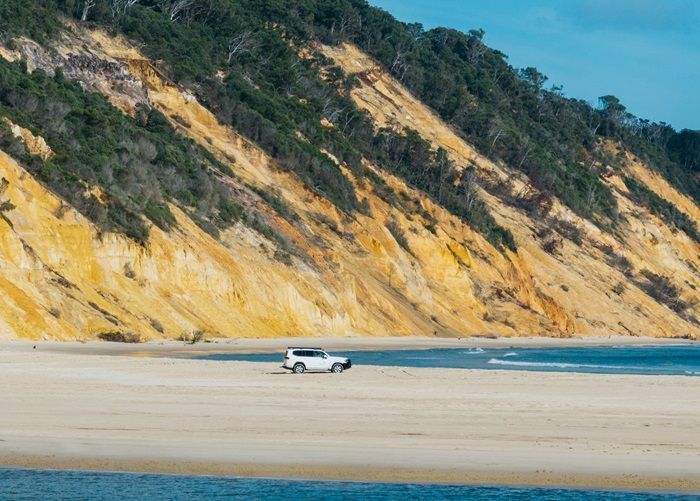 Wide shot of the orange cliffs of Rainbow Beach with a FleetCrew 300 Series Toyota LandCruiser parked on the sand