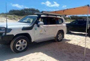 A shade awning set up on the beach, attached to a FleetCrew LandCruiser 300 series